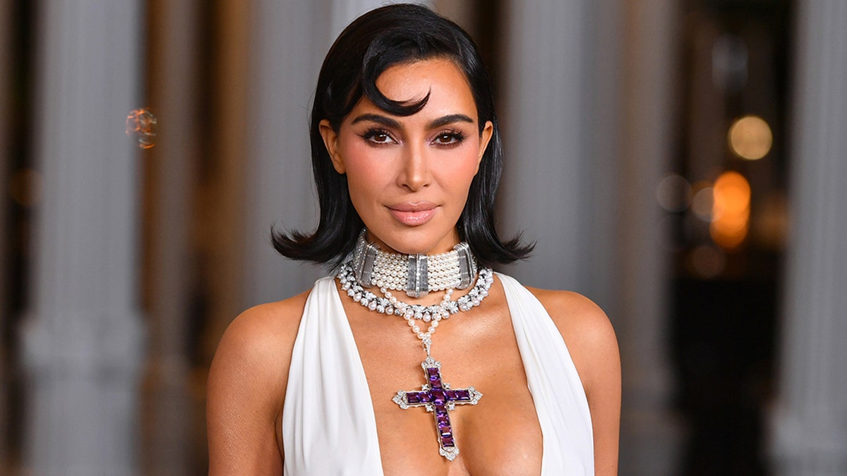 Kim Kardashian in a plunging white gown and a purple jeweled cross looks sultry on the carpet