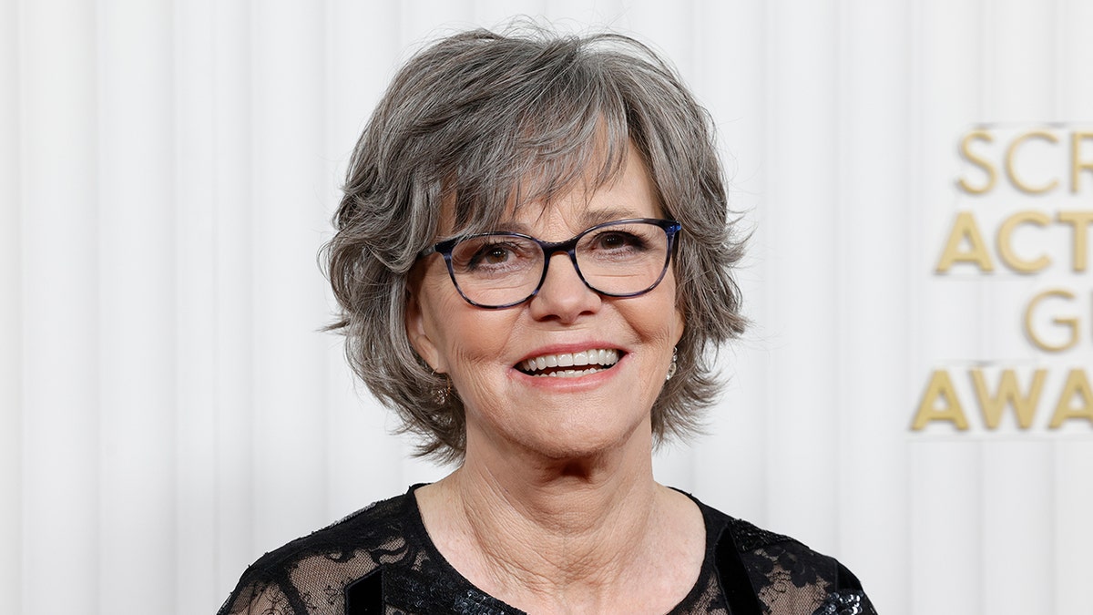 Sally Field in a black lacy dress and black framed glasses smiles and looks slightly up at the Screen Actors Guild Awards