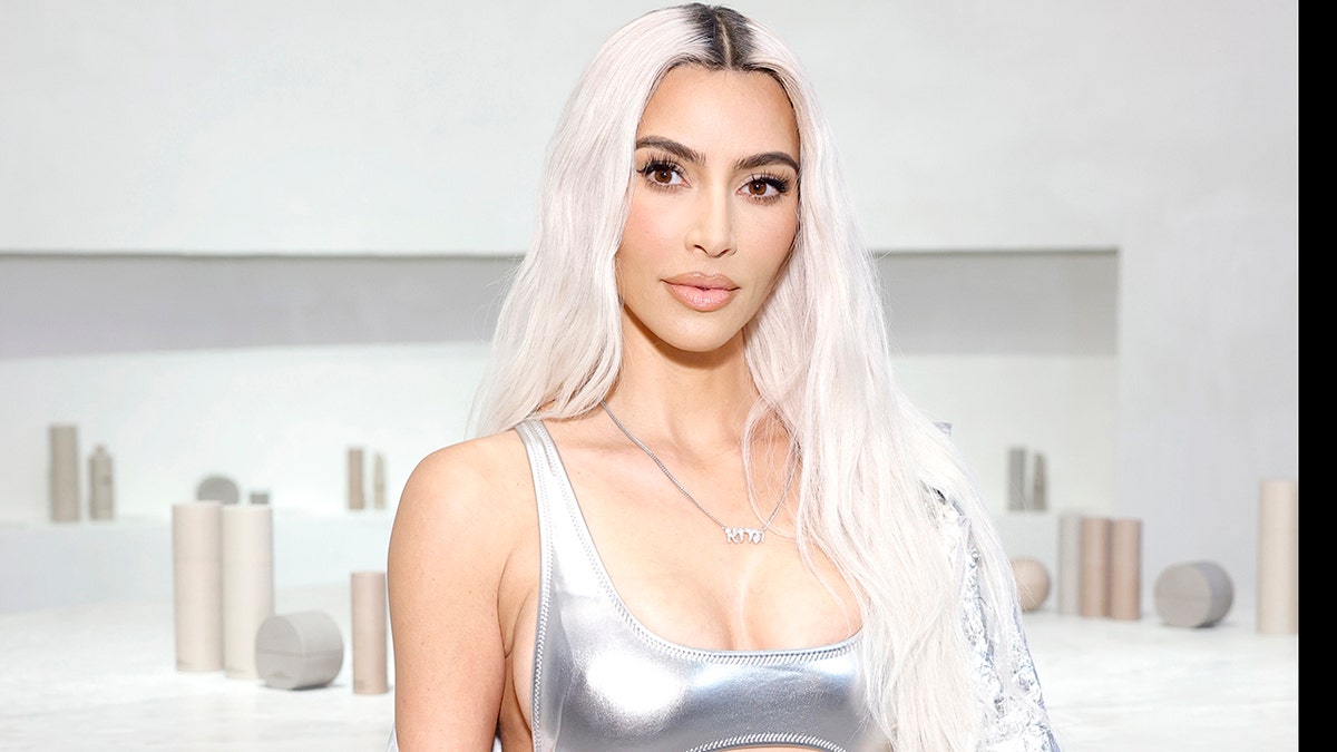 Kim Kardashian with platinum blonde hair in a silver outfit looks directly at the camera