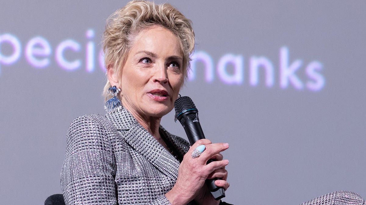 Sharon Stone in a blazer looks up while holding a microphone