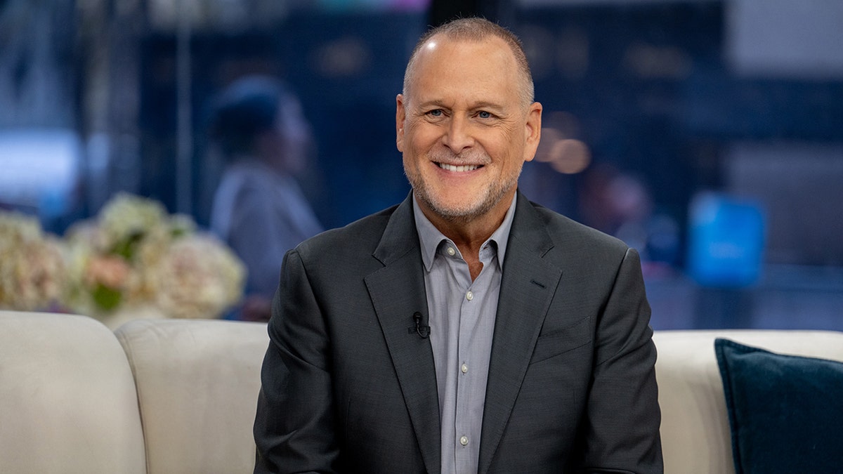 Dave Coulier in a dark grey suit smiles on 