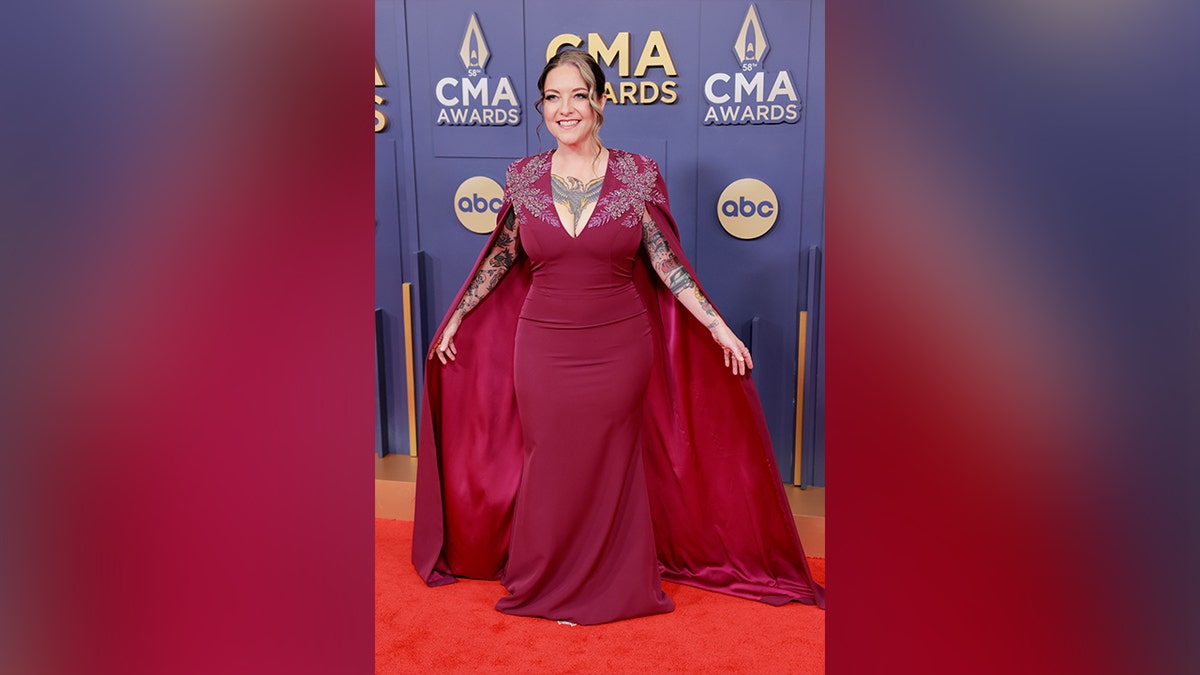 Ashley McBryde wore a red dress with a plunging neckline and a cape on the 2024 CMA Awards red carpet.