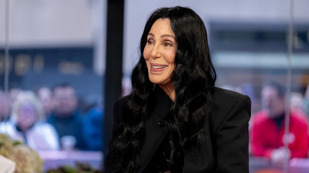 Cher in a black outfit smiles in a side-profile shot while on 