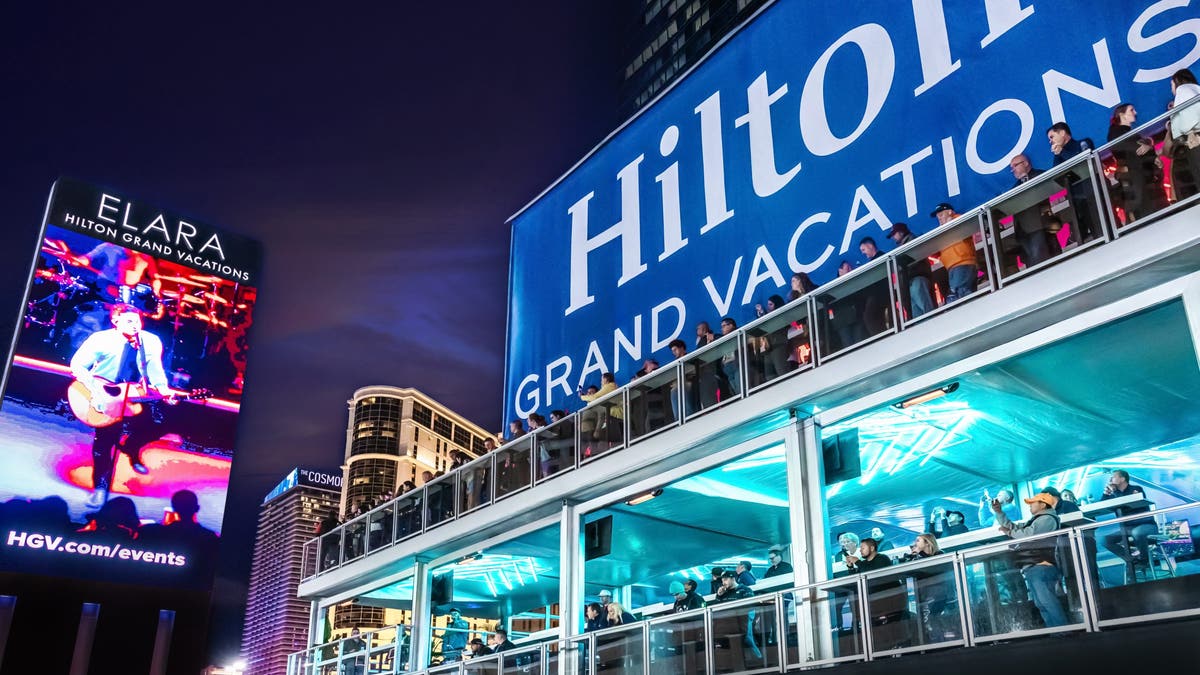 A large Hilton Grand Vacations sign with people looking out over a deck.