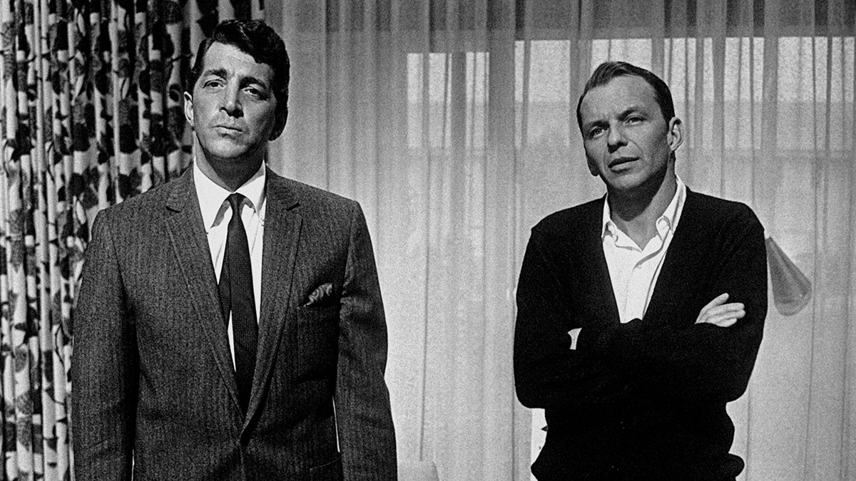 Black and white photo of Frank Sinatra in a suit and tie and Dean Martin with his arms crossed in a suit