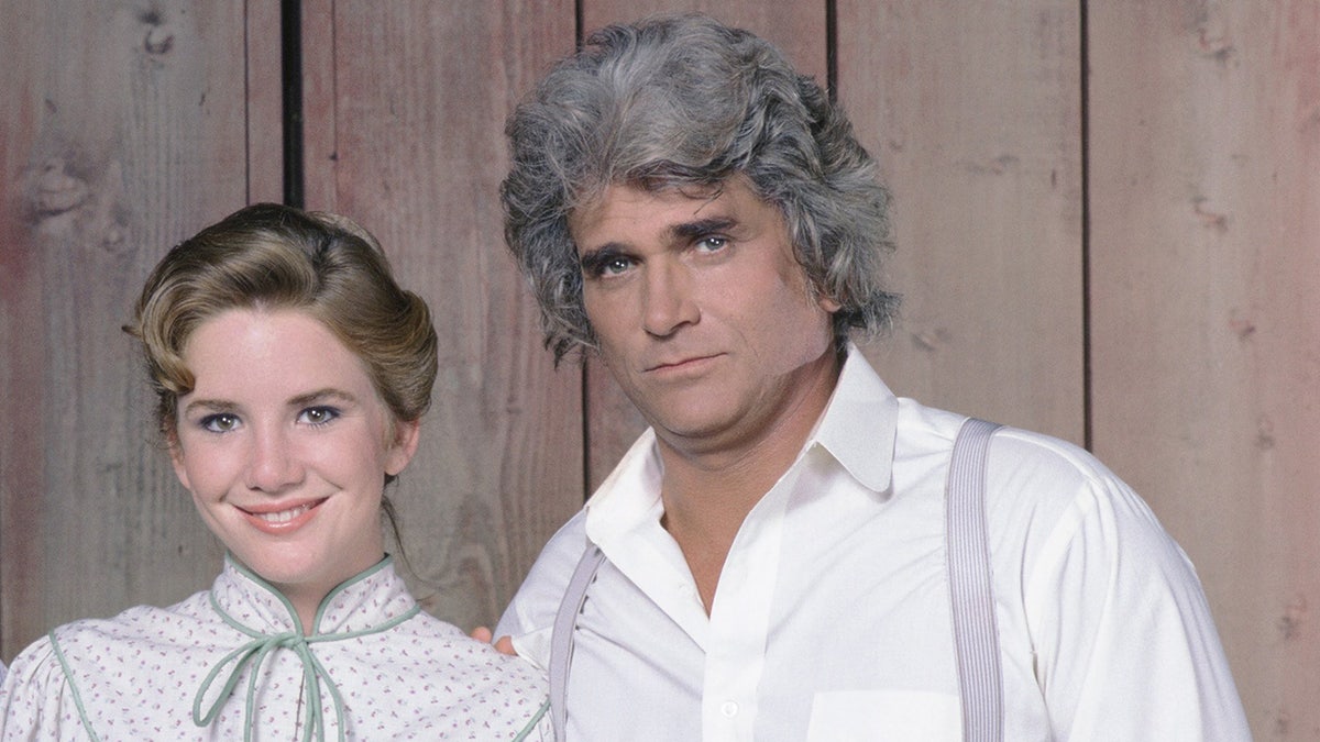 Melissa Gilbert smiles wearing a white blouse and green bow next to Michael Landon in a white shirt and purple suspenders in a photo from 