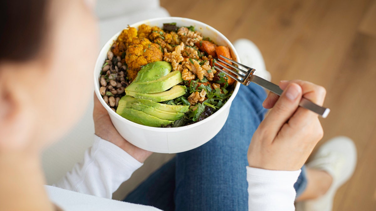 Woman eating fresh salad, avocado, beans and vegetables.