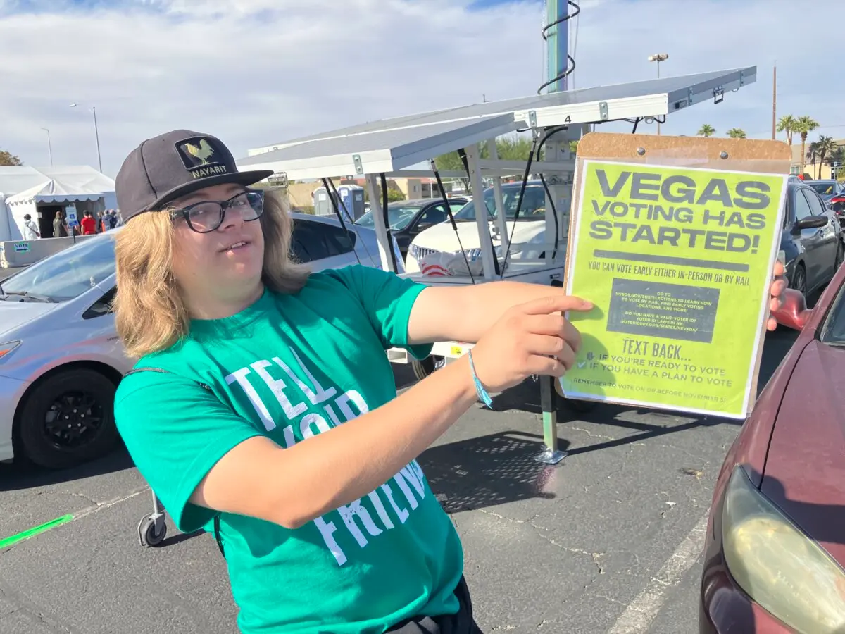 Jose, a 17-year-old volunteer with nonprofit, nonpartisan Democracy For All, displays what he shows people when he asks if they’re registered to vote in Nellis Crossing Shopping Center in Las Vegas, Nevada, on Nov. 1, 2024. (John Haughey/The Epoch Times)