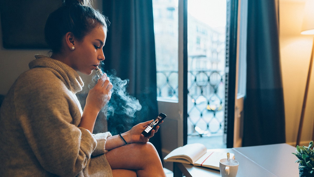 girl at home smoking e-cigarette on phone