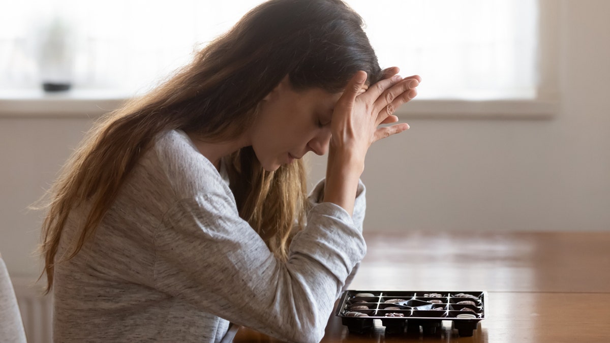 Sad girl sits at table with box of chocolates