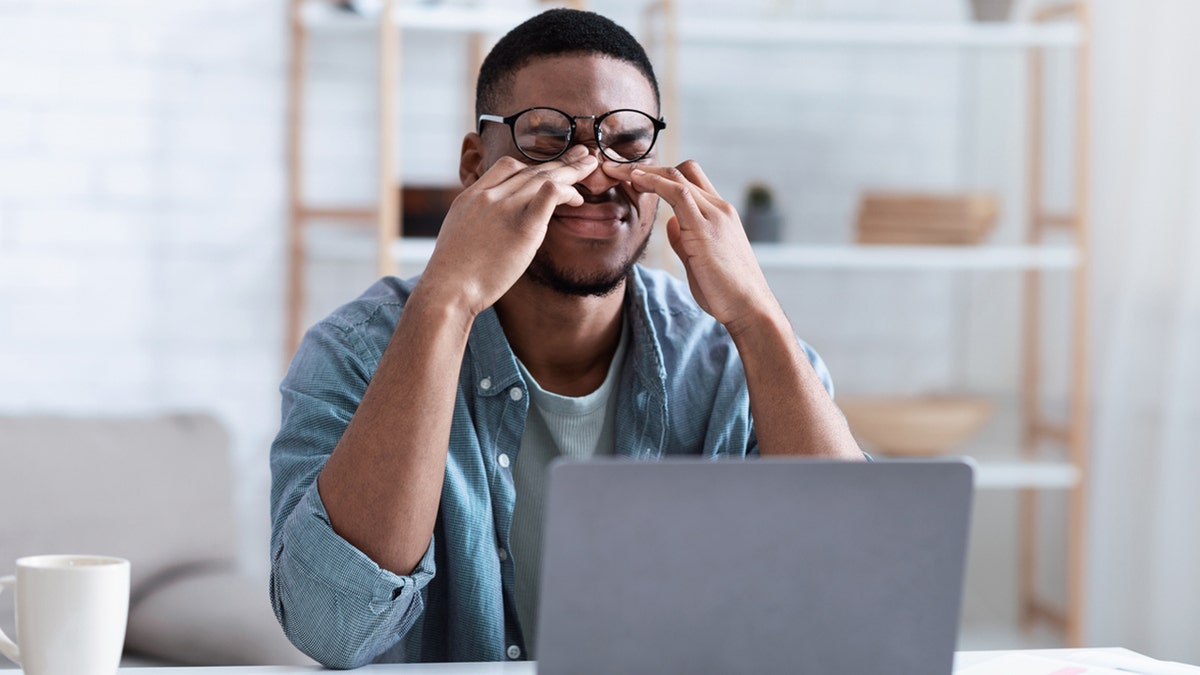 Man rubs his eyes while working on a laptop