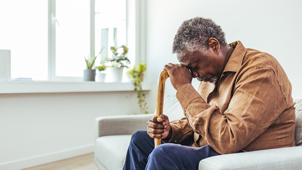 elderly man sitting alone at home with his walking cane