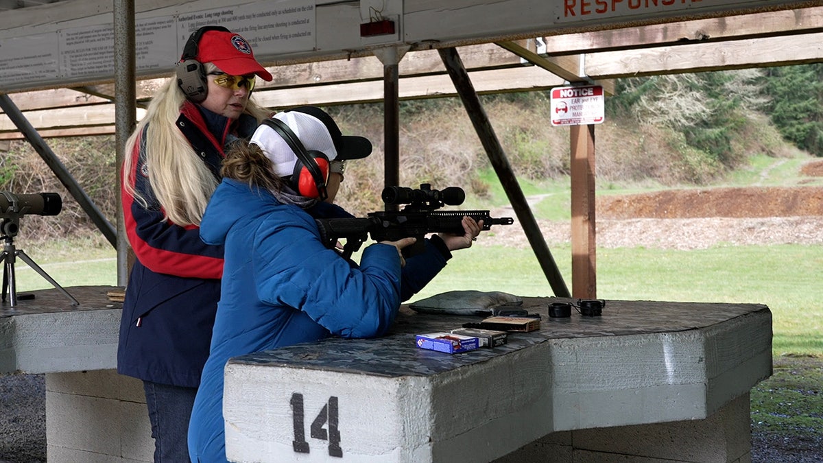 Firearms instructor helps woman aim AR-15 at outdoor rifle range