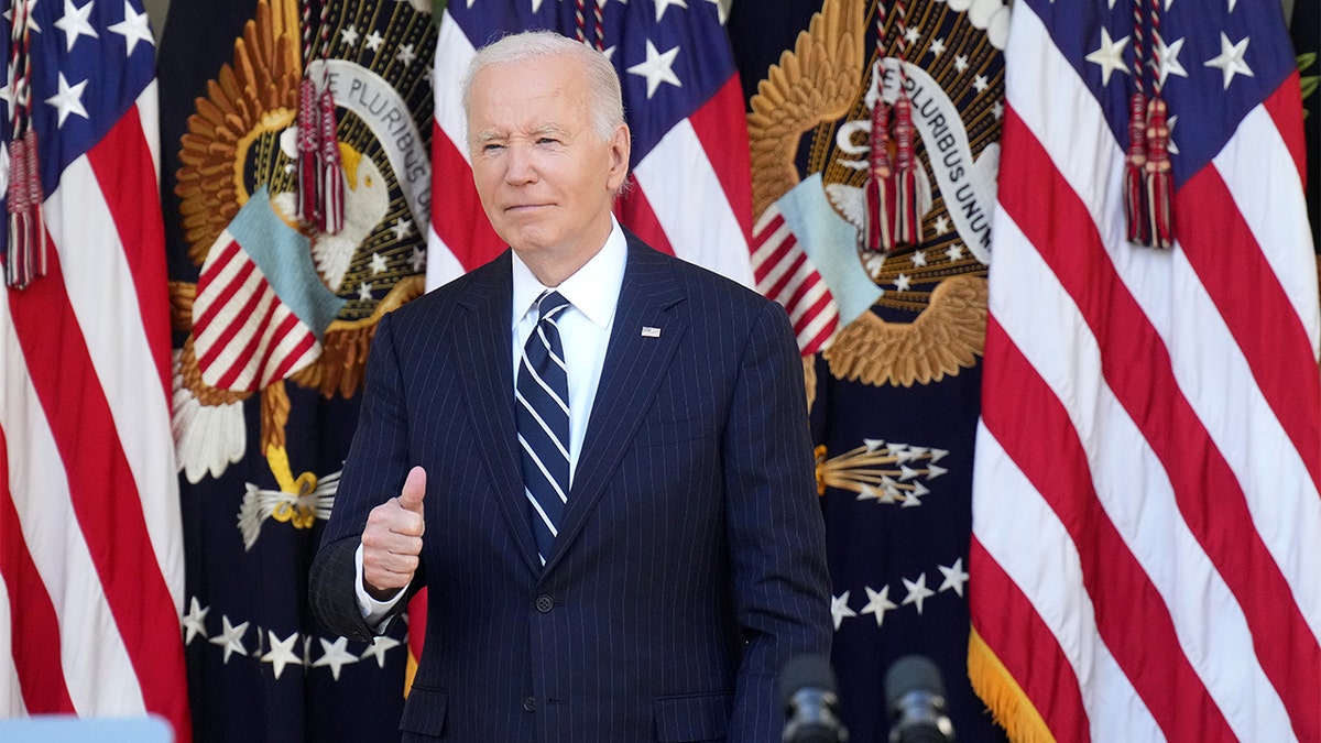 President Biden giving thumbs-up in front of US, presidential flags