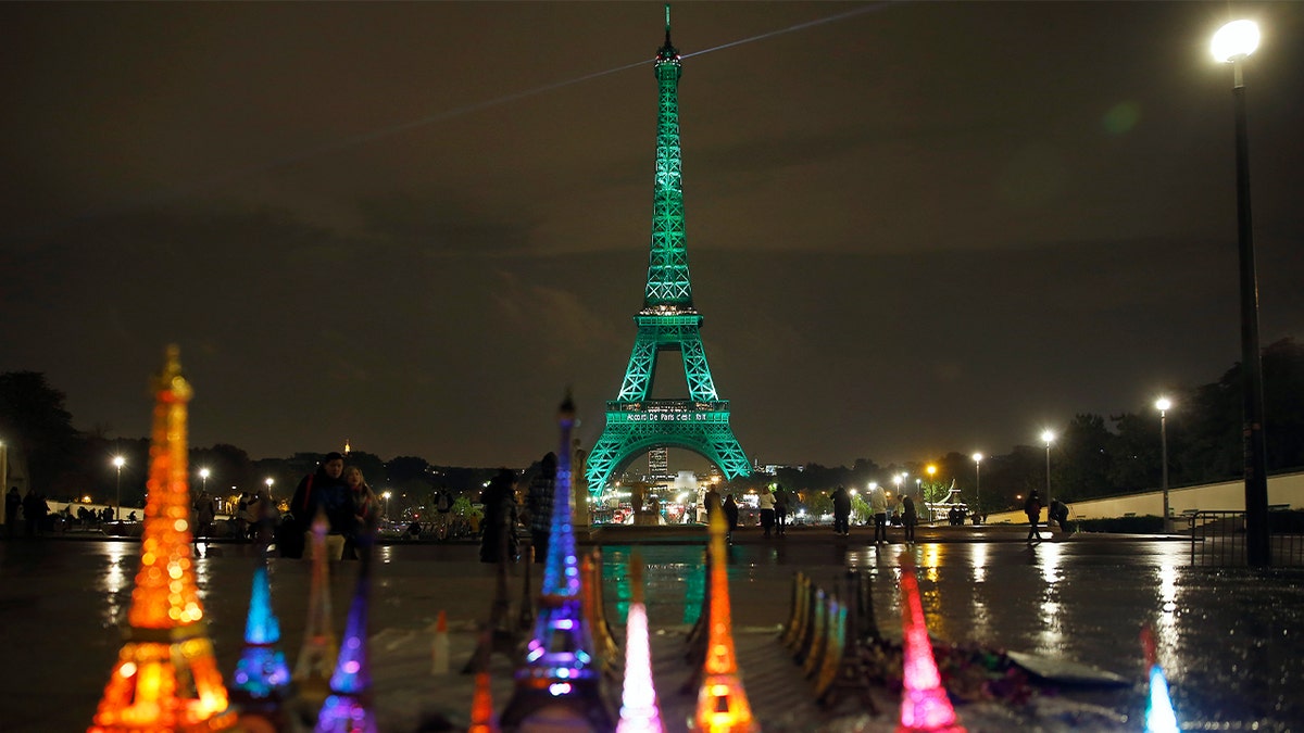 Small gift-size Eiffel Towers are seen in front of the Eiffel Tower illuminated in green with the words 