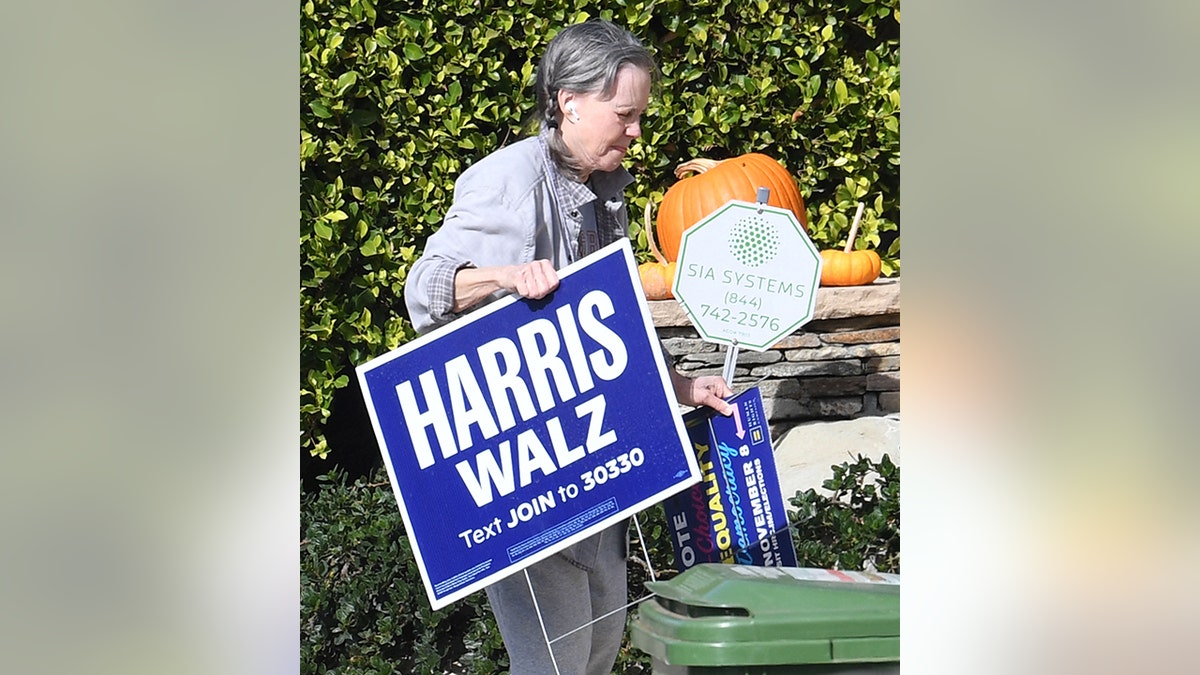 Sally Field with pumpkins in the background walks with a Harris-Walz sign to the trash