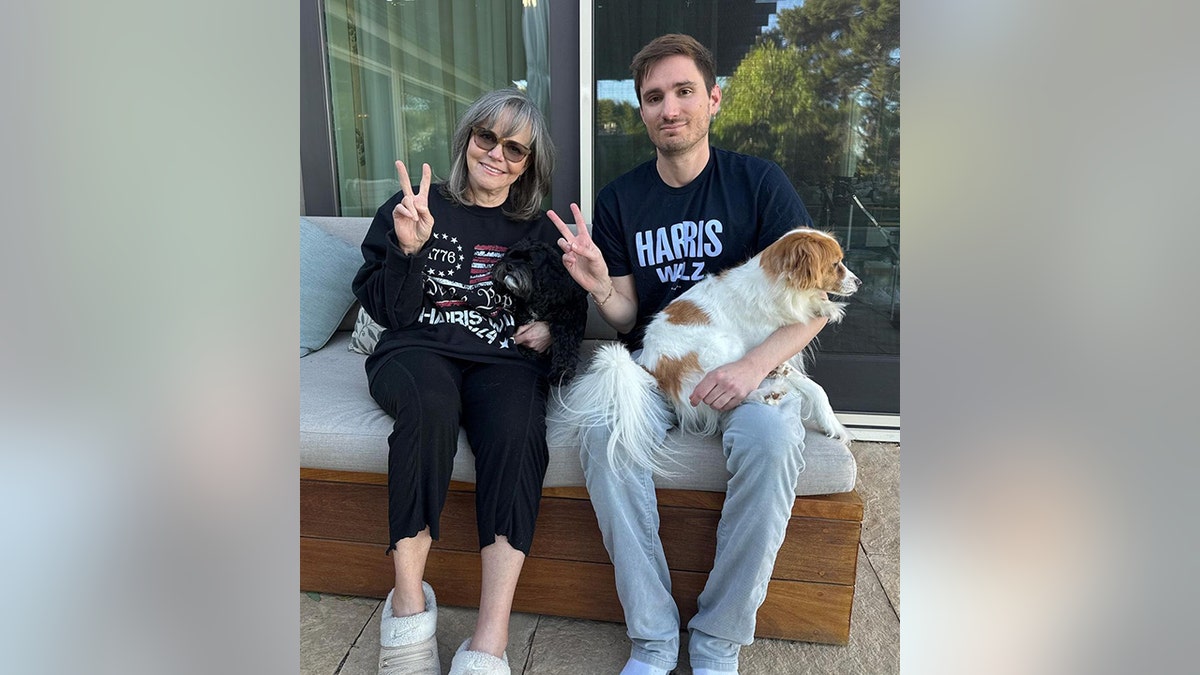 Sally Field in a black shirt and bottoms throws up a piece sign with her son Sam and two dogs