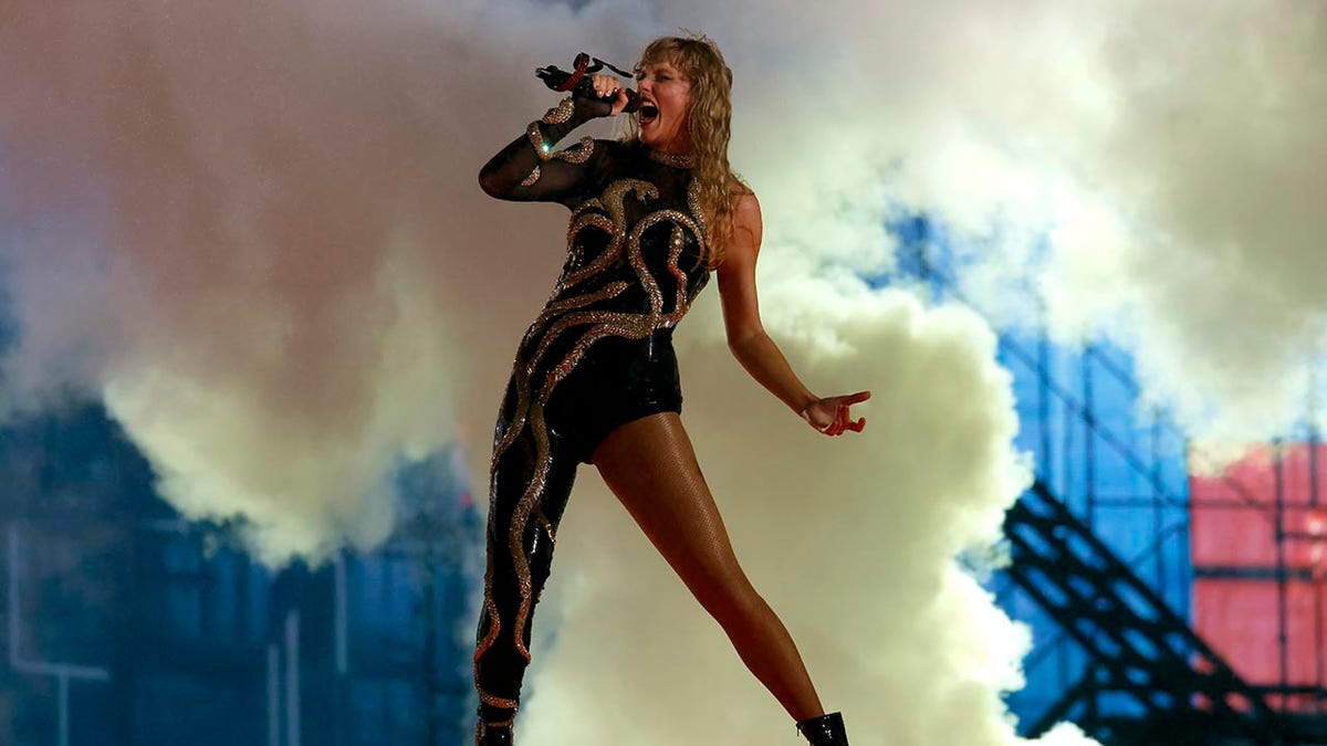 Taylor Swift in her new 'Reputation' outfit, a jumpsuit with only one leg fully covered, sings dramatically into the microphone