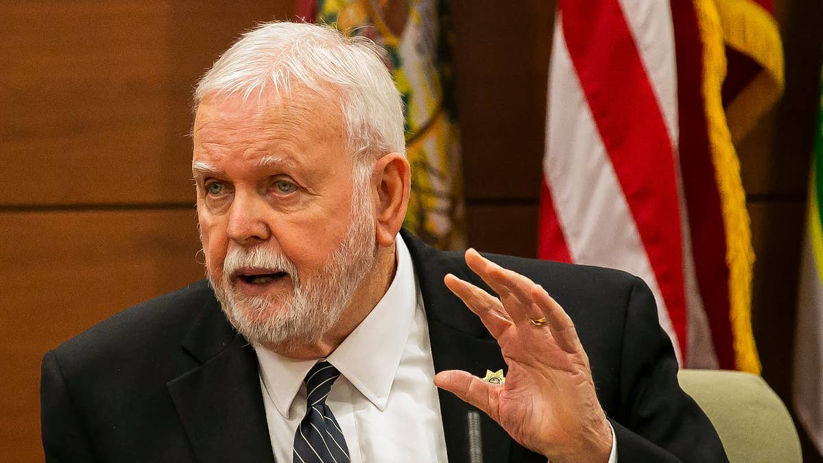 Ron McAndrew testifies in court, wearing a dark suit, with white hair and a beard