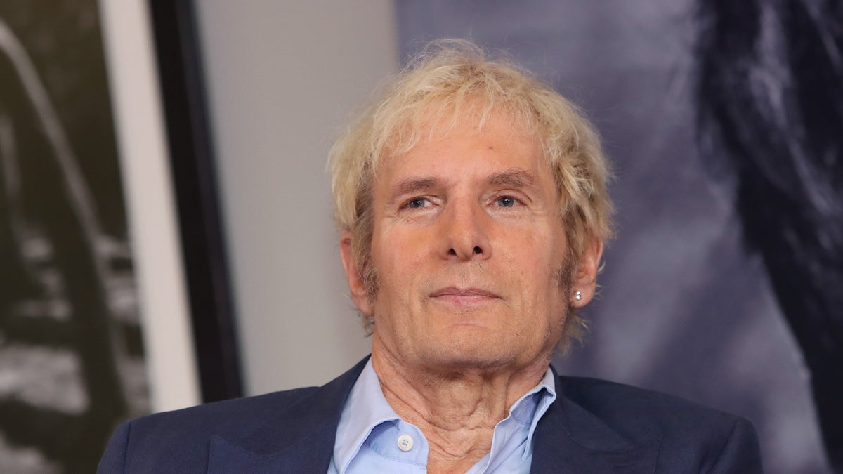 Michael Bolton wearing a navy blazer and a button down light blue shirt.