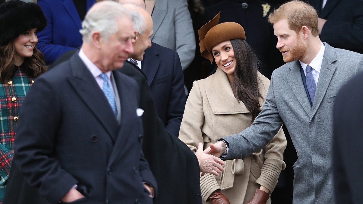 King Charles walking ahead of Prince Harry and Meghan Markle as they shake hands and greet people.