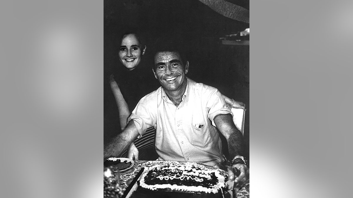 Anne Serling standing behind her dad wearing a white shirt and smiling in front of a birthday cake.