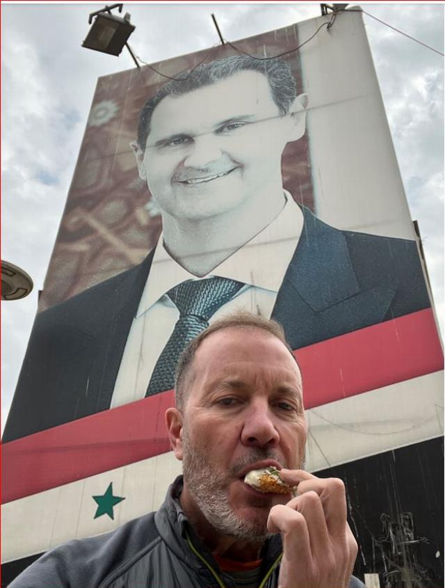 Joondeph enjoying falafel in Syria under the giant Assad poster