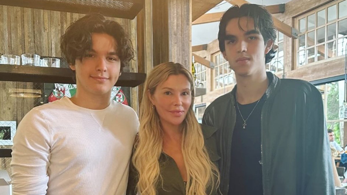 Brandi Glanville stands in the middle of her two sons Jake Austin in a white long-sleeve shirt and Mason in a green jacket and black shirt