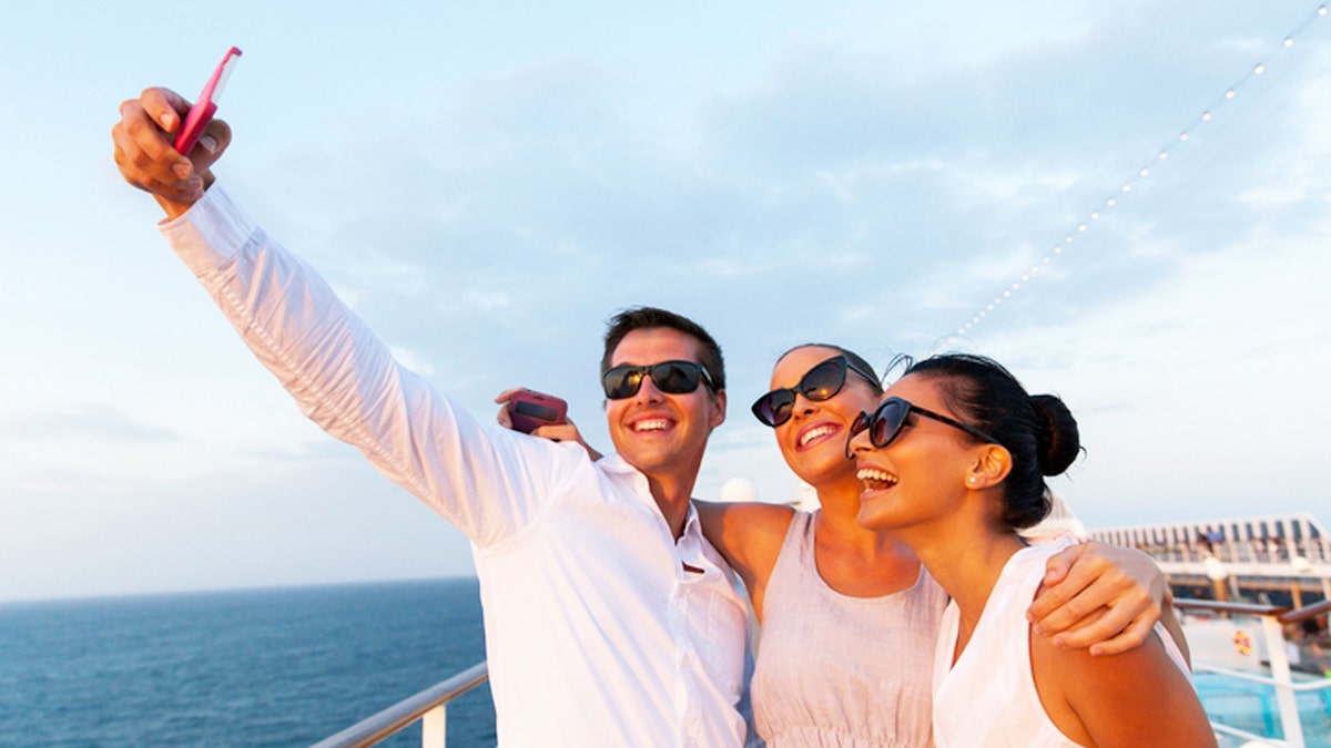 group of friends taking self portrait using smart phone on cruise