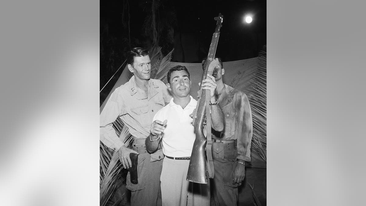 Dick York smiling at Rod Serling holding a rifle.