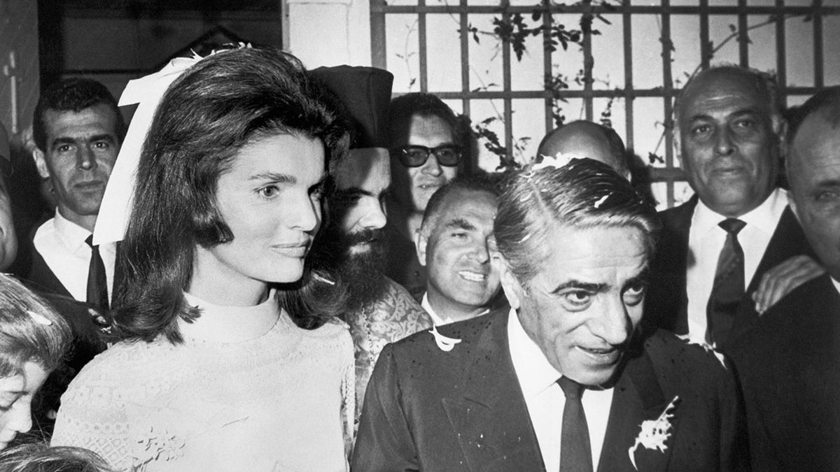 A close-up of Jackie Kennedy and Aristotle Onassis walking in the middle of a crowd on their wedding day.