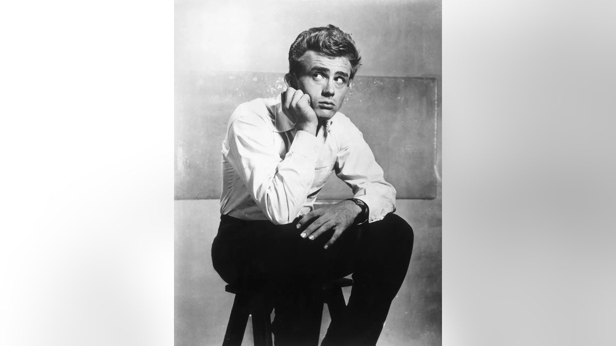 James Dean sitting on a stool with a white shirt and black pants.