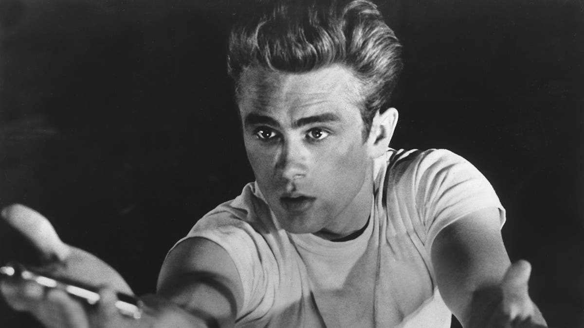 James Dean with his arms stretched out wearing a white shirt.