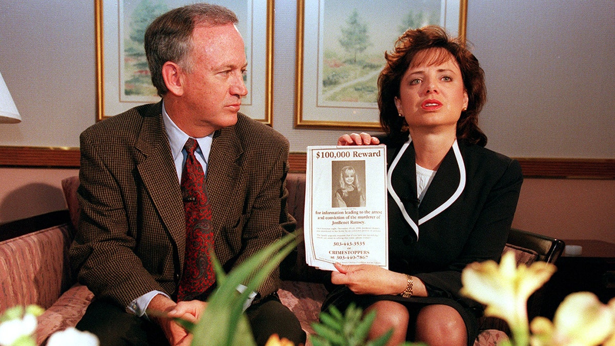 John Ramsey and his wife Patricia sitting next to each other as Patricia holds a reward sign.