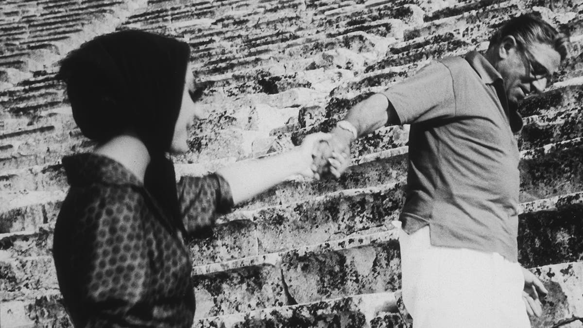 Aristotle Onassis holding the hand of Maria Callas as they climb up stairs.