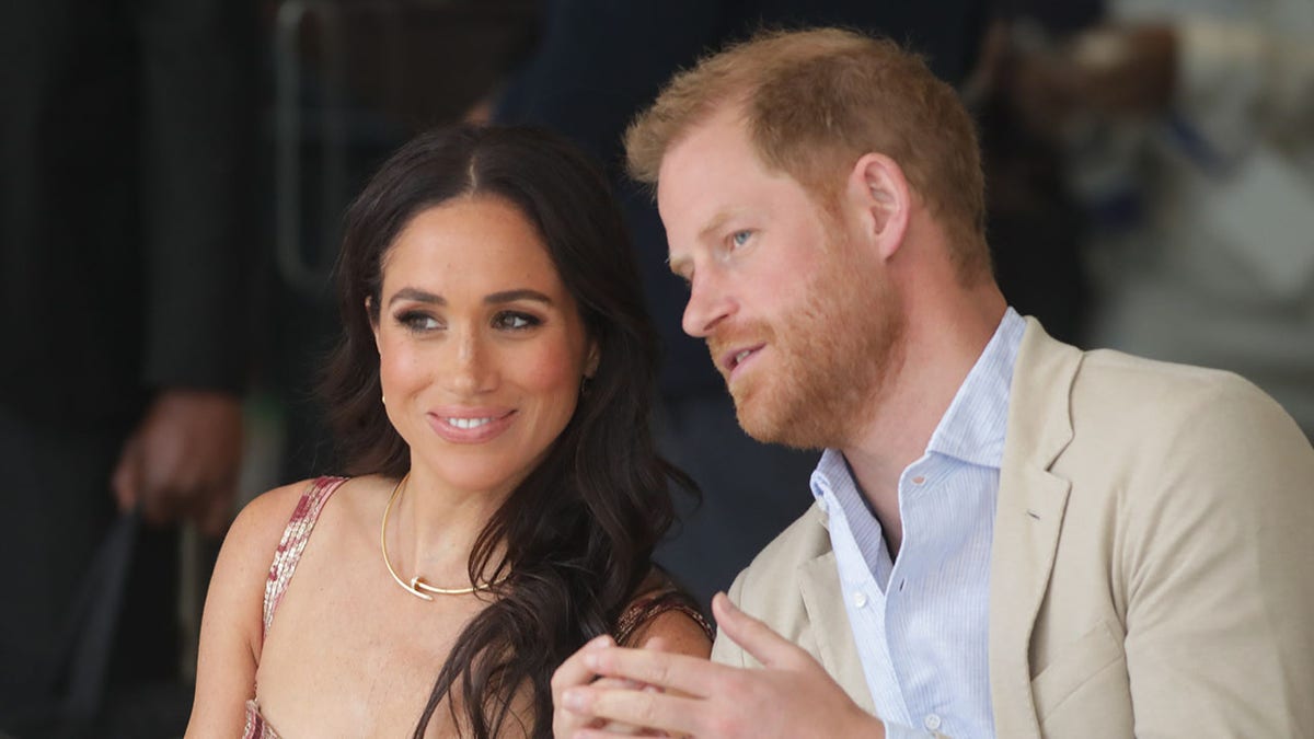 Prince Harry chatting with Meghan Markle who looks on smiling.