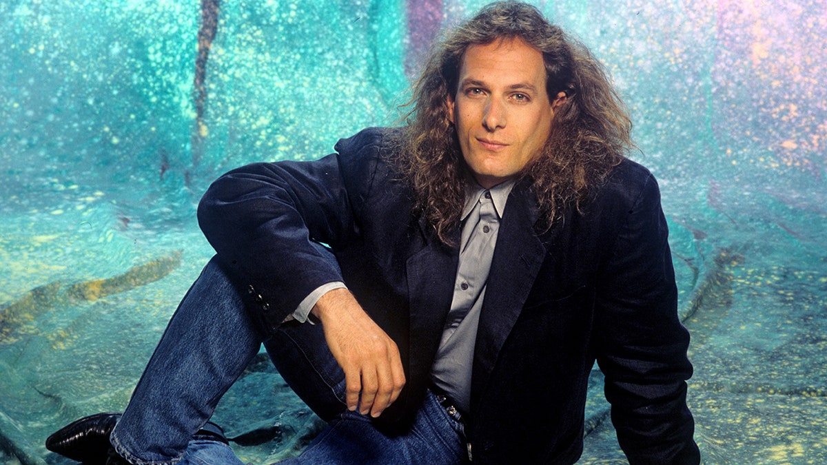 Michael Bolton in a dark blue blazer, gray shirt and blue jeans.