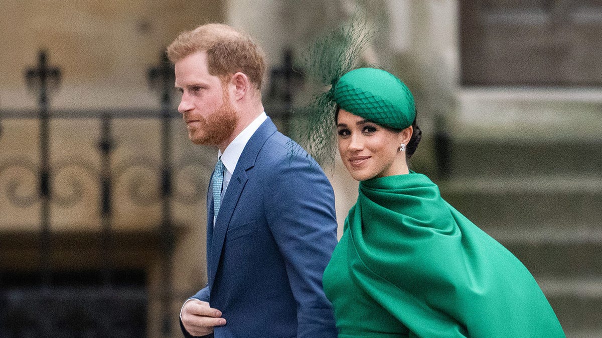 Meghan Markle wearing a green dress with a matching hat walking next to Prince Harry in a light blue suit.