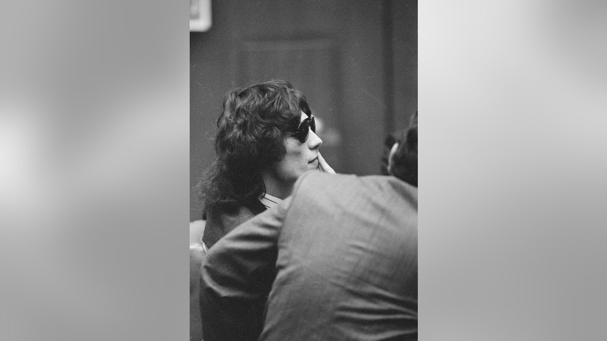 A side profile of Richard Ramirez looking at a court room with sunglasses.