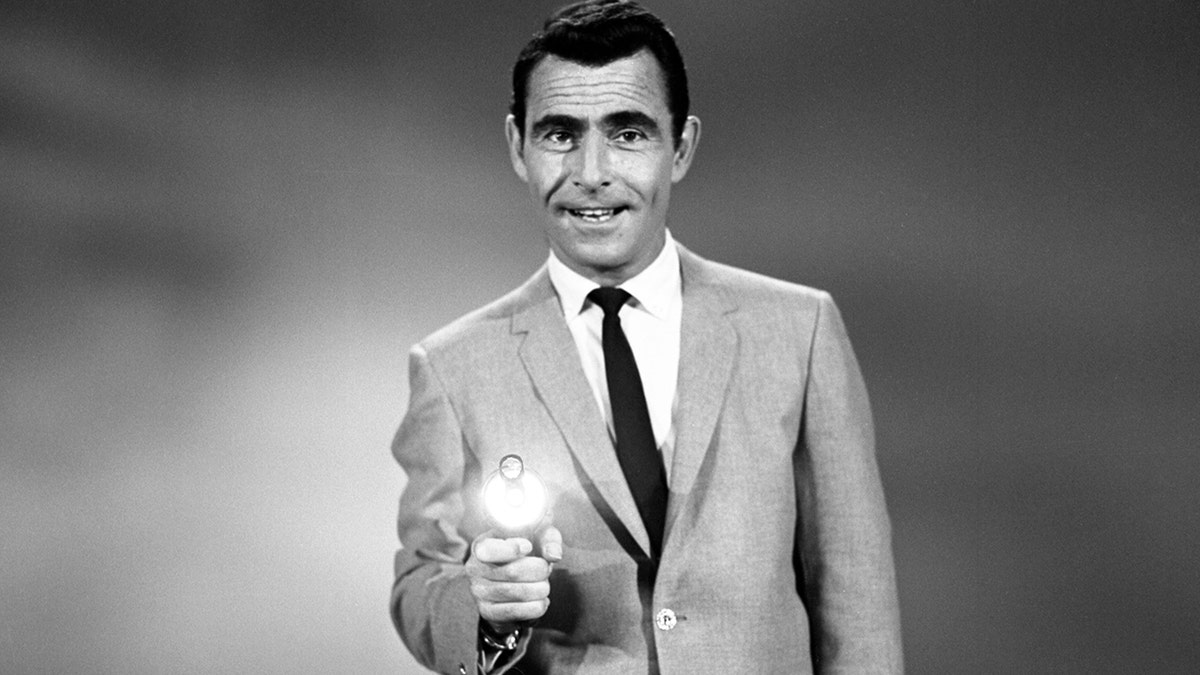 Rod Serling shooting a gun while wearing a suit.