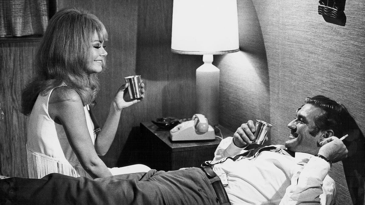 Rod Taylor and his female co-star having a drink in a bedroom.