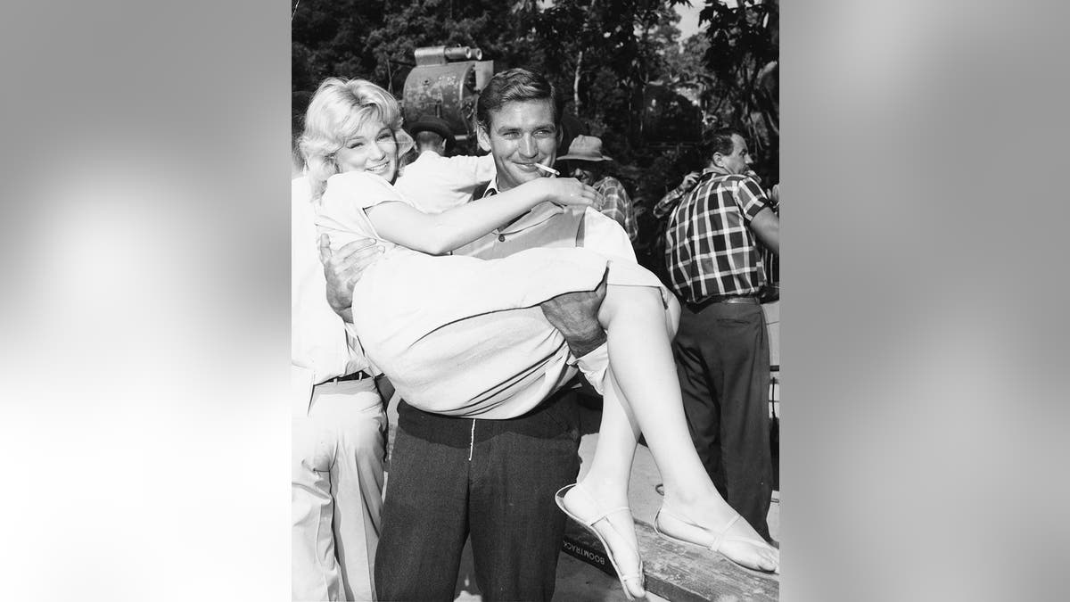 Rod Taylor holding a smiling blonde on set.