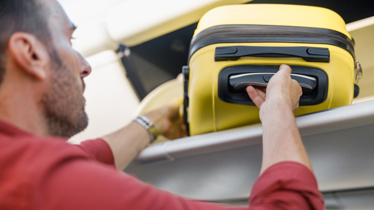 Man pulling out hand luggage from compartment while traveling by plane