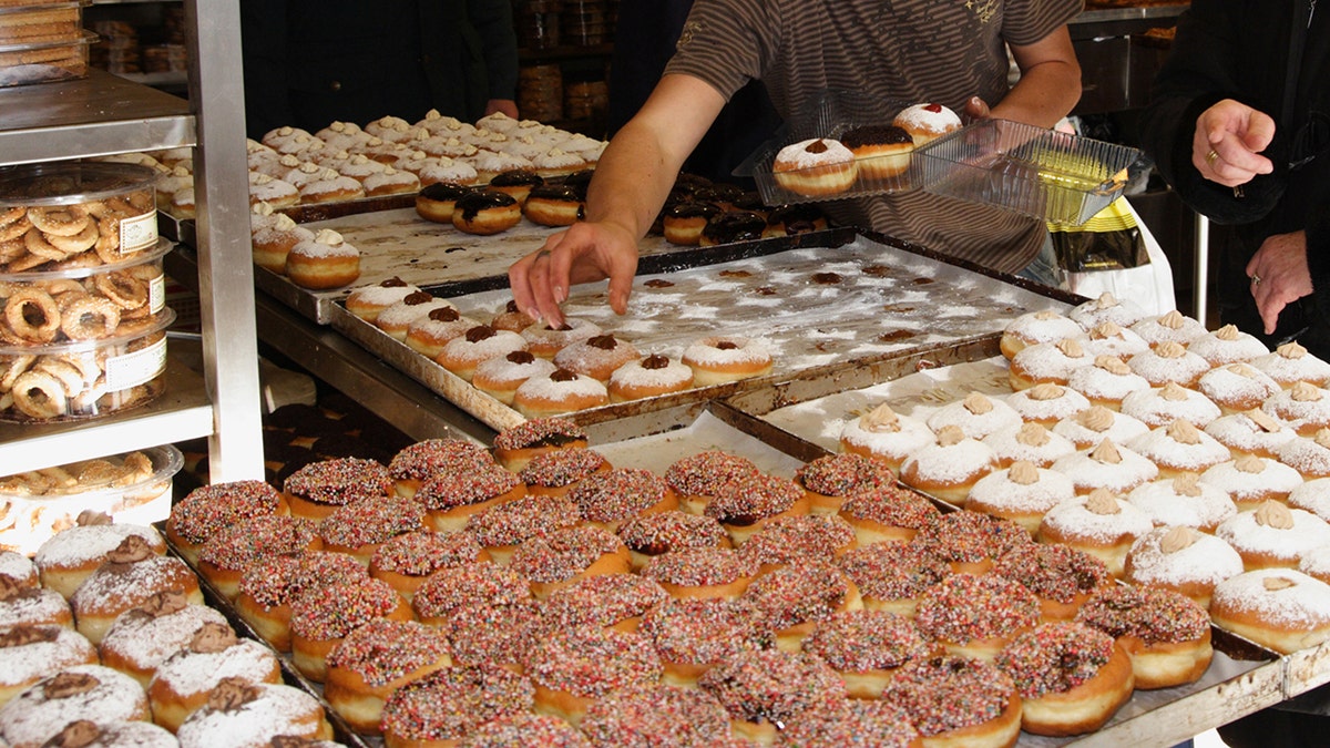 As an unidentified woman stands by, a man shops for sufganiyah. 