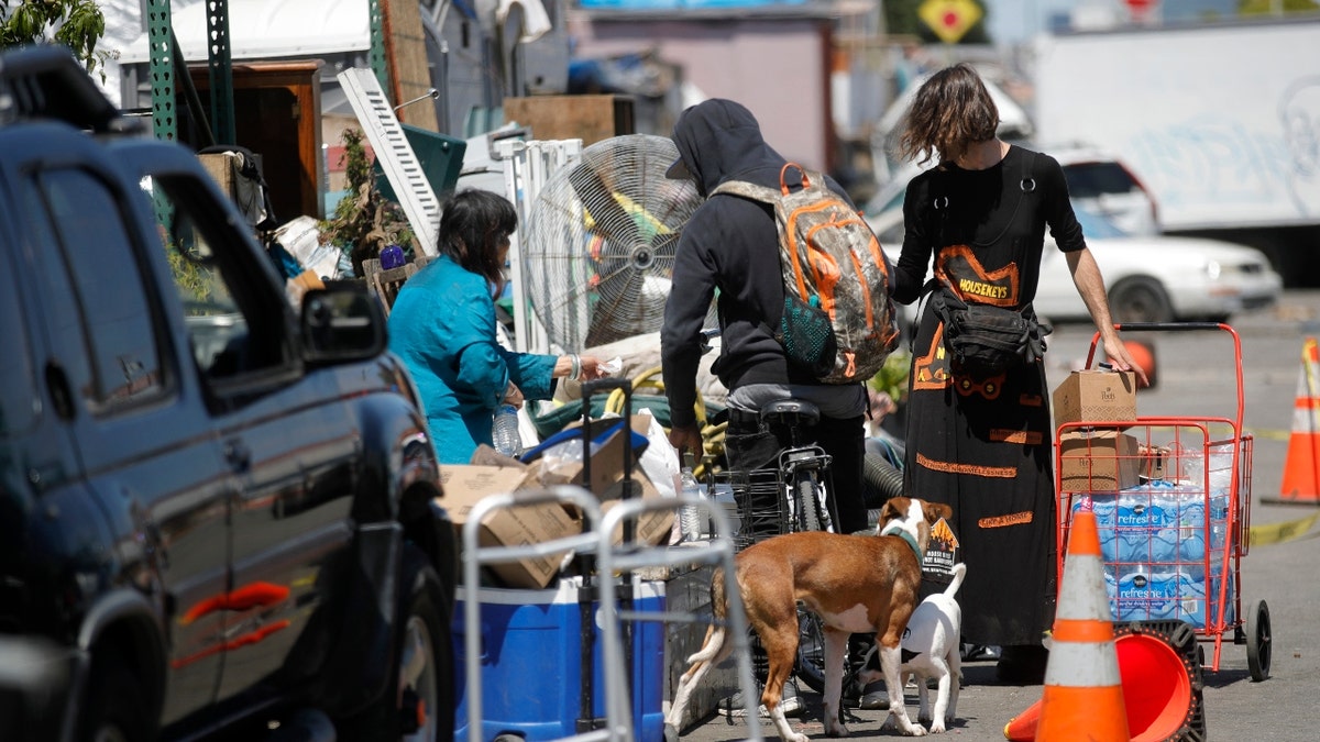 Jaz, who preferred to not give their last name, right, delivers food and beverages for residents of a homeless encampment along East 12th Street near 16th Avenue in Oakland, Calif., on Wednesday, May 15, 2024.