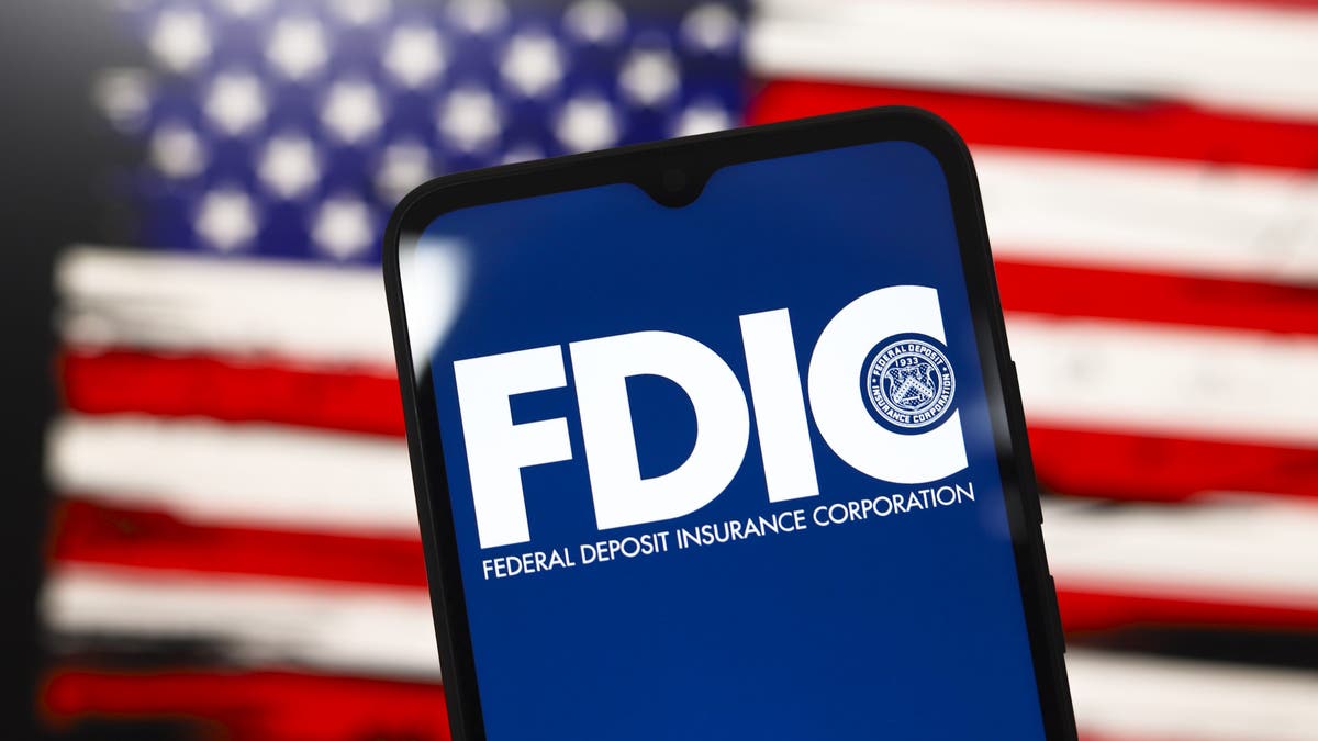 The United States Federal Deposit Insurance Corporation logo appears on the screen of a smartphone, and in the background, the flag of the United States is on the computer screen in Reno, Nevada, on Dec. 3, 2024.