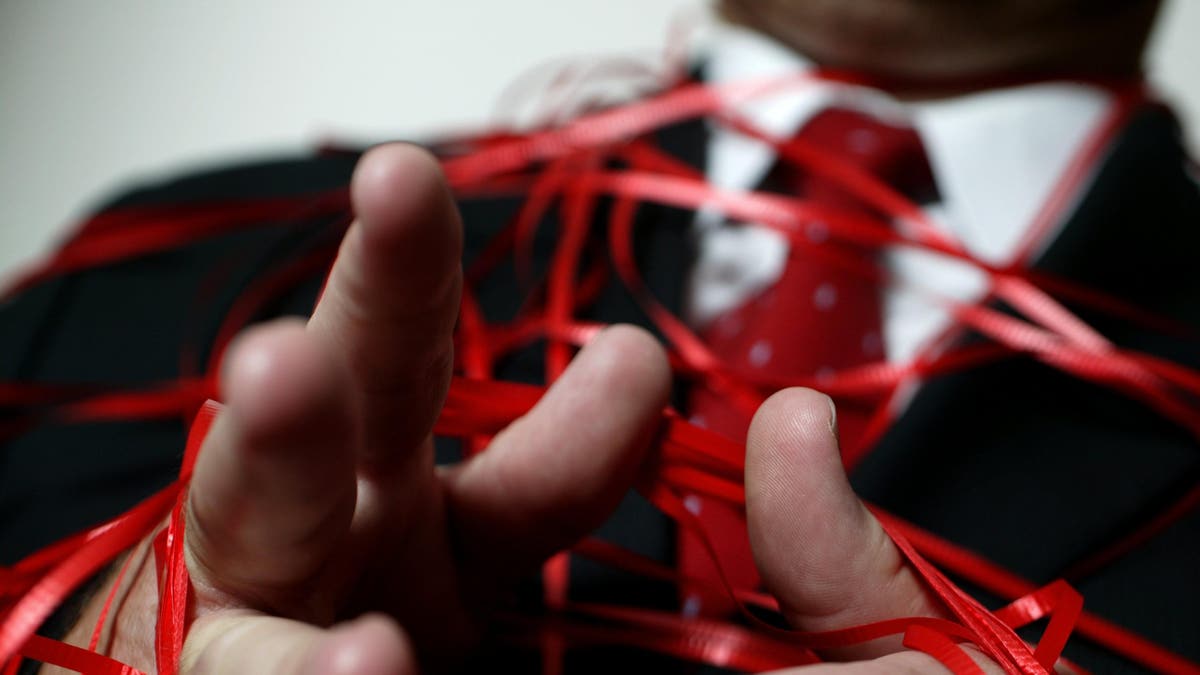 A businessman is wrapped in red tape.