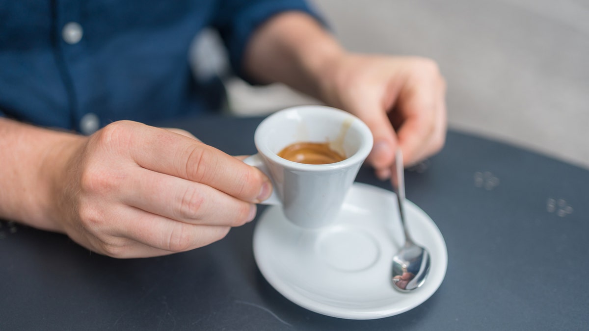 A man's hand picks up a cup of espresso.