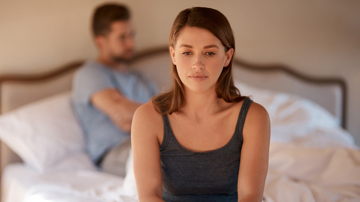 woman sitting on the edge of the bed with man in bed