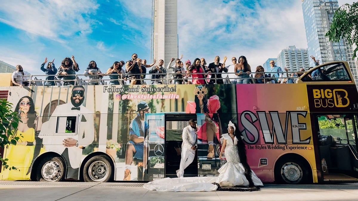 Wedding guests and bride and groom posing in front of customized hop-on, hop-off bus.